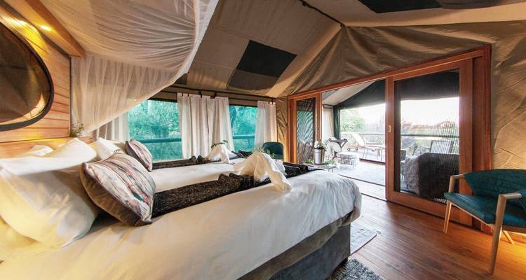 Intérieur de tente luxueux avec lits et rideaux, face à une vue dégagée sur la nature.