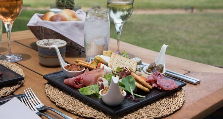 Gourmet meal setup with drinks on a wooden outdoor table.