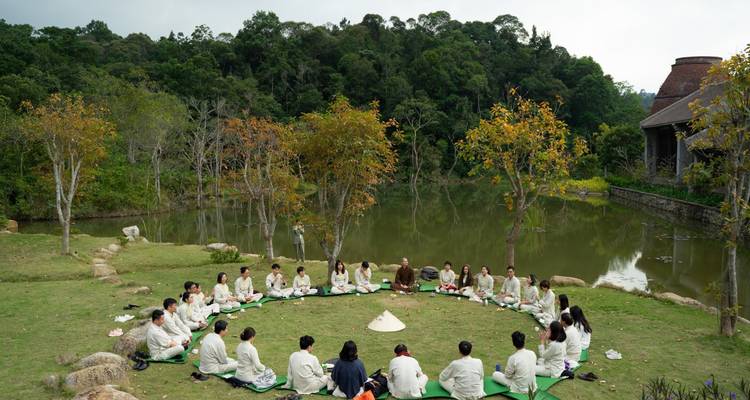 People gathered in a circle near a scenic pond