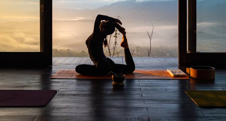 Silhouet van een vrouw die yoga beoefent binnenshuis met een schilderachtig uitzicht op de bergen.