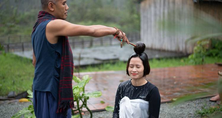 Man pours water over seated woman outdoors.