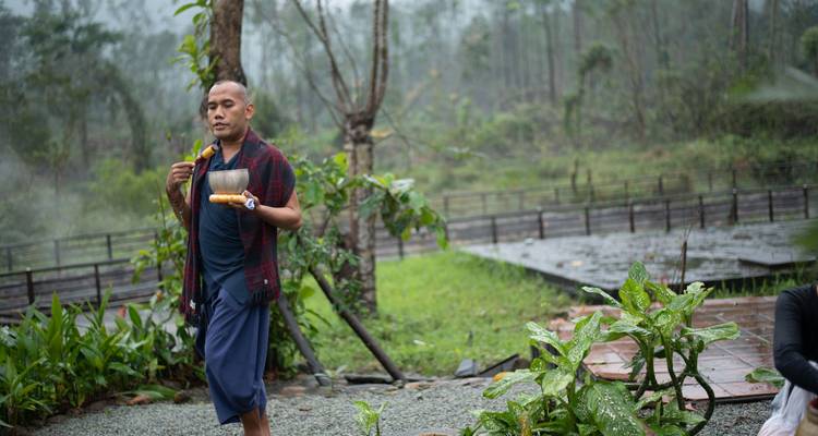 Man walking with a singing bowl in a garden setting.
