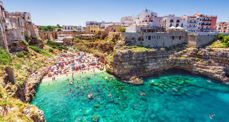 Cala de playa abarrotada con aguas turquesas cristalinas y casas en acantilados en Polignano a Mare.