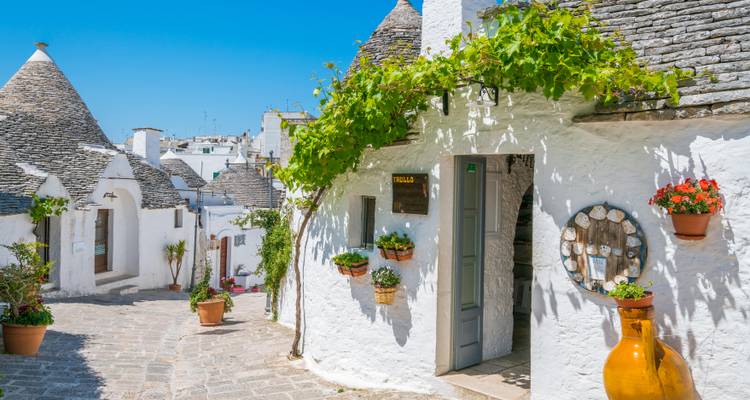 Las icónicas casas trulli encaladas con techos cónicos a lo largo de una soleada callejuela de piedra en Alberobello.
