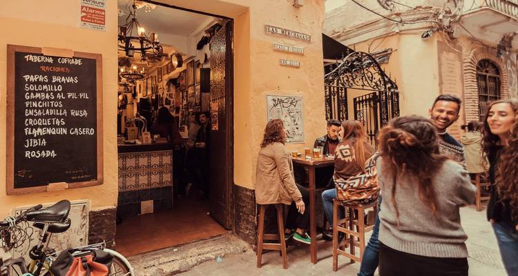 La gente disfruta de bebidas afuera de un acogedor bar de tapas en una estrecha calle andaluza.