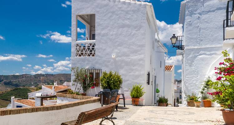 Casas encaladas y un callejón adoquinado con vistas a colinas ondulantes bajo un cielo azul brillante.