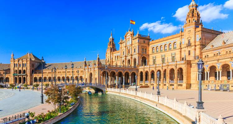 La gran Plaza de España de forma semicircular en Sevilla se refleja en su canal bajo un cielo brillante.