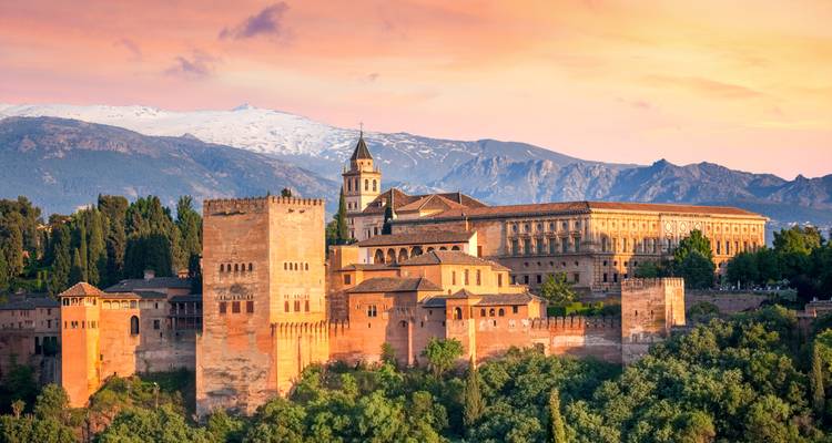 El complejo palaciego de la Alhambra brilla con tonos de atardecer contra la Sierra Nevada cubierta de nieve.
