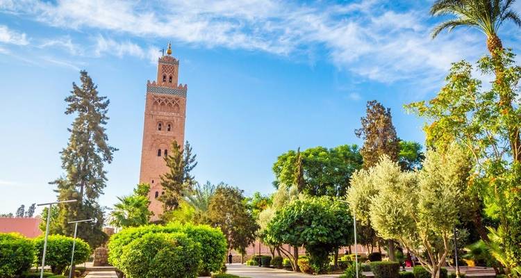Minarett umgeben von üppigem Grün unter blauem Himmel.
