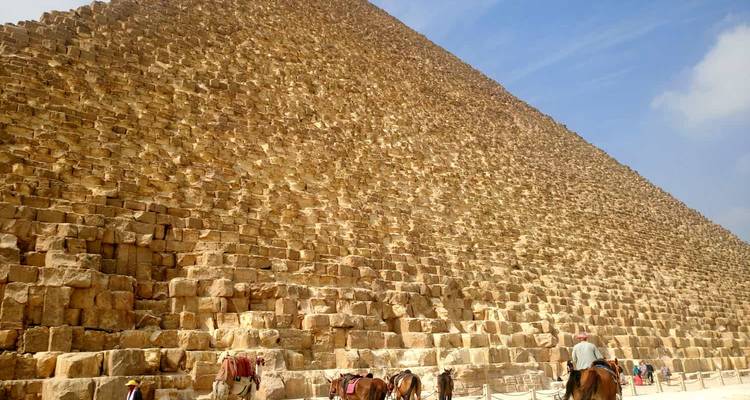 Base of a large pyramid with people riding horses.