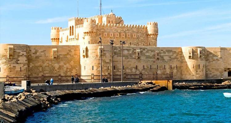 Ancient fortress by the sea with people walking on the pier.