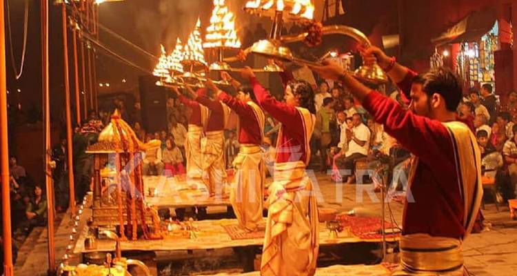 Sacerdotes realizando Ganga Aarti con lámparas encendidas mientras los fieles observan, superpuesto con el texto grande 'KASHI YATRA'