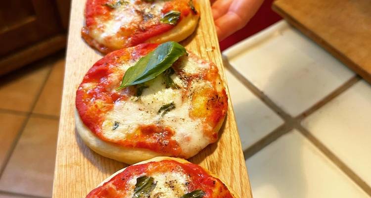 Mini pizzas on a wooden board with a leaf garnish.