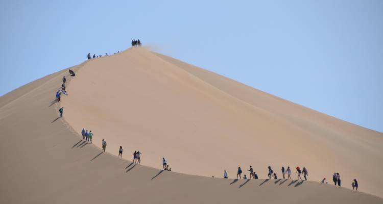 Longue file de personnes grimpant une dune de sable.