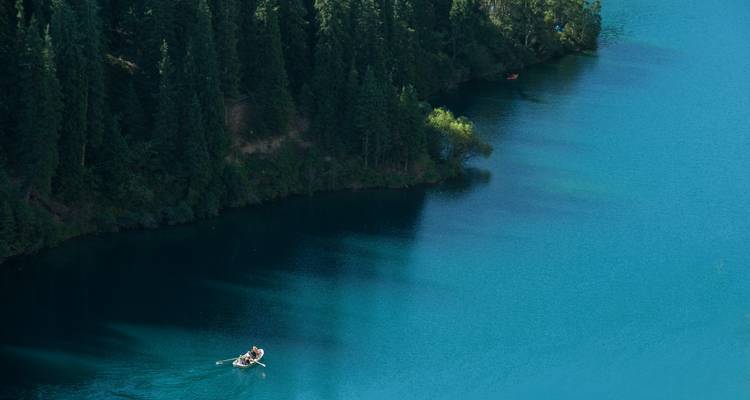 Personne ramant dans un bateau sur un lac serein entouré d'arbres.
