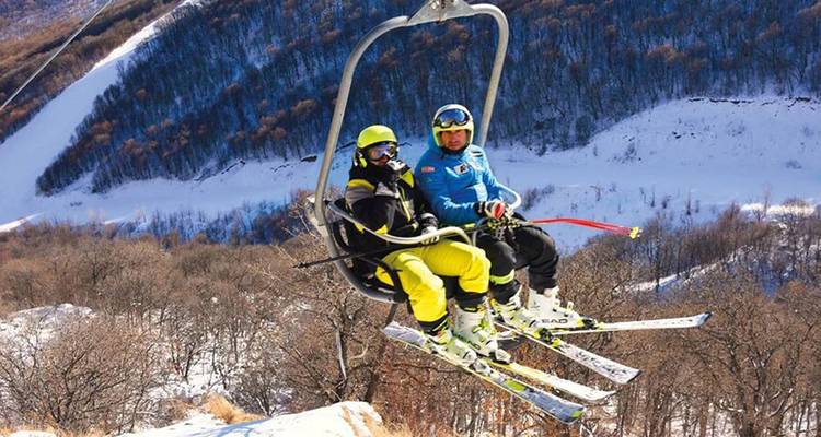 Two people on a ski lift overlooking snowy slopes.