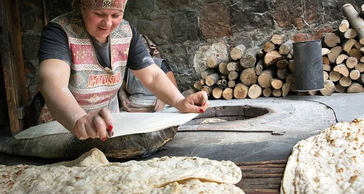 Woman preparing traditional bread with wood logs in the background.