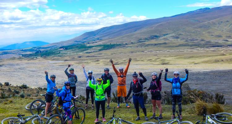 Groupe de cyclistes posant avec les mains levées dans une région montagneuse.