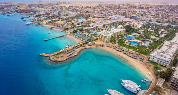 Vue aérienne de la ligne côtière de la ville de Hurghada avec des complexes touristiques, une marina, des baies turquoise et des bateaux.
