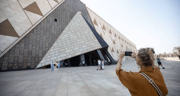 Un visiteur photographie la façade moderne angulaire du Grand Musée égyptien avec des motifs pyramidaux.