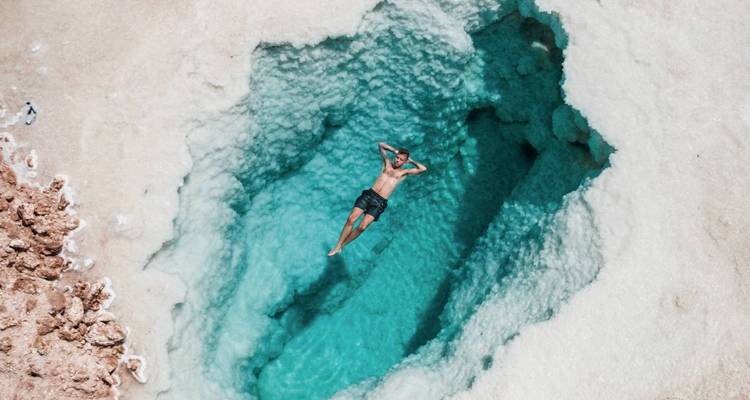 Person schwimmt in klarem blauen Wasser umgeben von weißen Salzformationen.