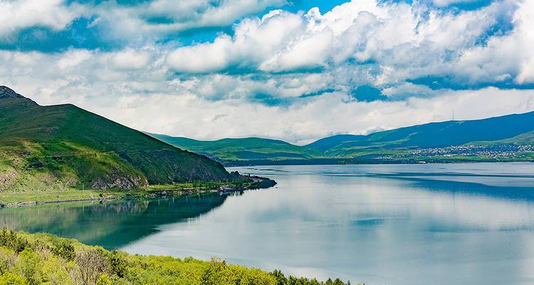 A calm lake surrounded by green hills under a cloudy sky