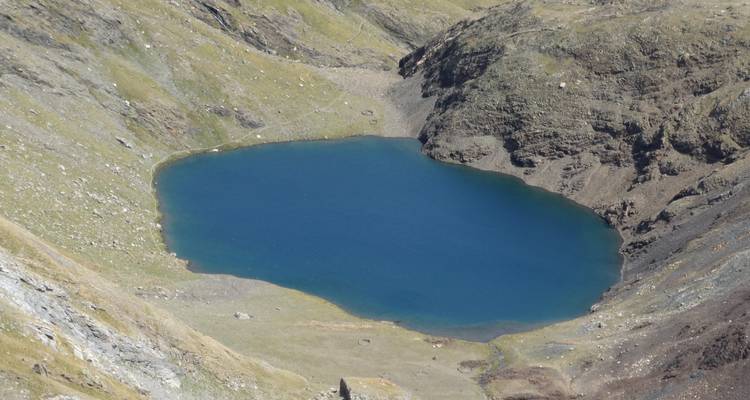 Un lac alpin d'un bleu profond entouré d'un terrain accidenté.