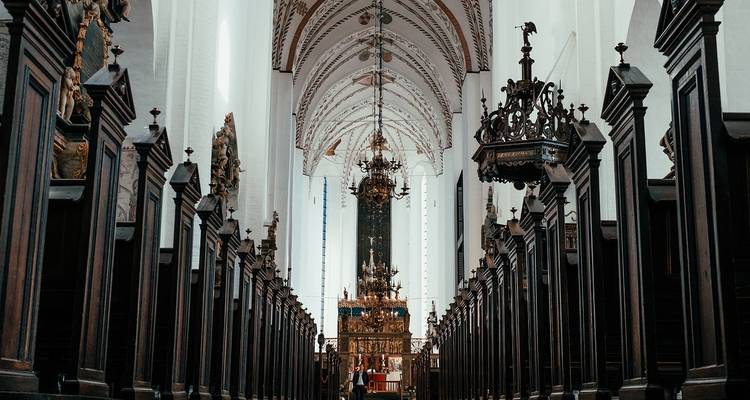 Innenraum einer prächtigen gotischen Kathedrale mit Gewölbedecken, ornamentalen Kronleuchtern und einem fernen vergoldeten Altar.