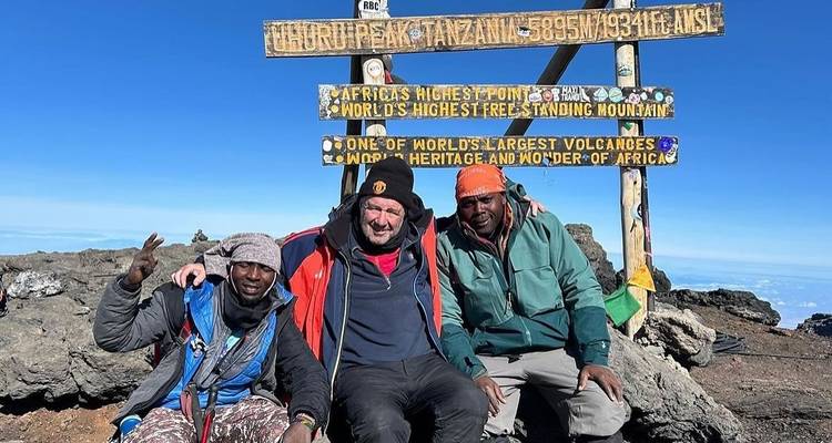 Drie mensen op een bergtop met borden die grote hoogte aangeven.