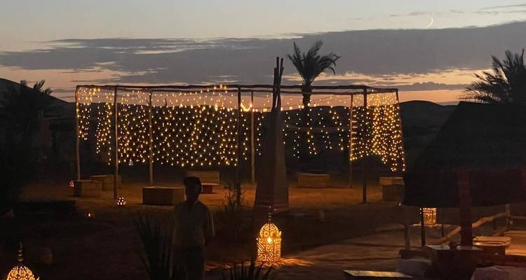 Las luces de hadas brillantes cuelgan en el patio de un campamento en el desierto mientras el atardecer se posa, con una figura recortada contra la luz.