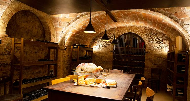 Rustic wine cellar with arched brick ceilings, shelves of bottles and a table set for tasting.