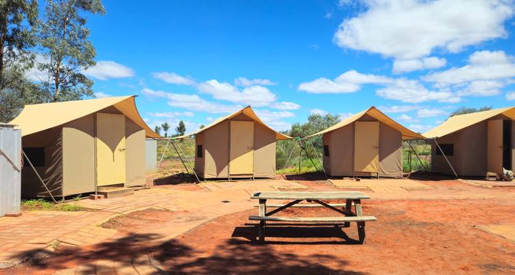 Fila de cabañas de tienda de campaña con mesa de picnic en un campamento de tierra roja bajo nubes brillantes