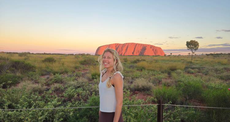 Mujer sonriente posando con Uluru bañado en cálida luz del atardecer de fondo