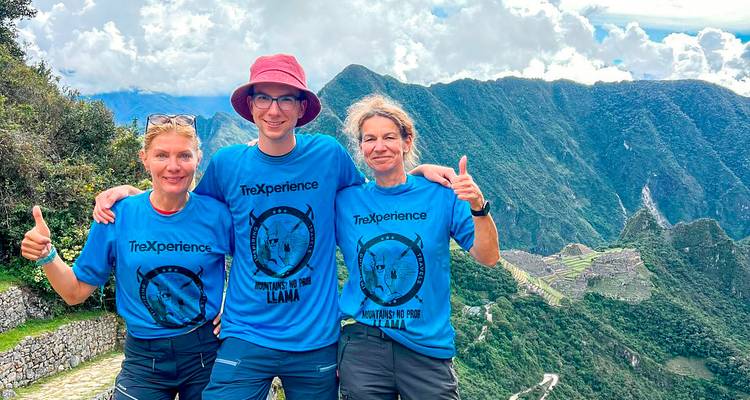Drei Wanderer in passenden Hemden lächeln mit Machu Picchu im Hintergrund.