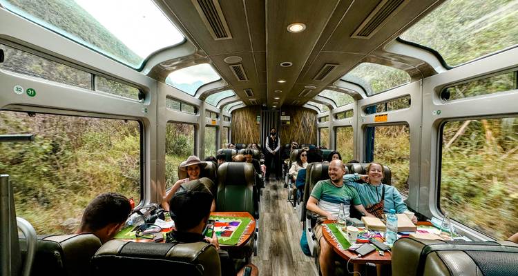Interieur van een panoramische trein met glazen dak met reizigers die chatten, eten en genieten van het uitzicht op het weelderige Andese landschap.