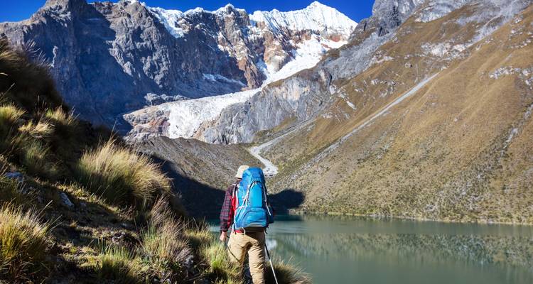 Persoon die wandelt langs een meer met besneeuwde bergen op de achtergrond.
