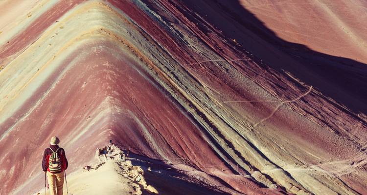 Persoon op een bergtop met een panoramisch uitzicht op Rainbow Mountain.