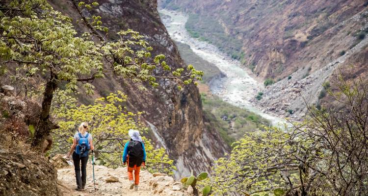 Deux randonneurs sur un sentier de montagne avec une vallée fluviale en contrebas.