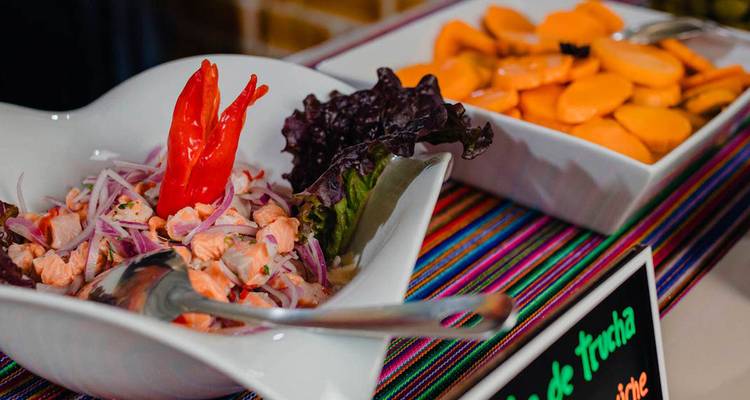 Gros plan d'un plat de buffet présentant un ceviche avec du piment et des oignons à côté d'autres plats locaux.