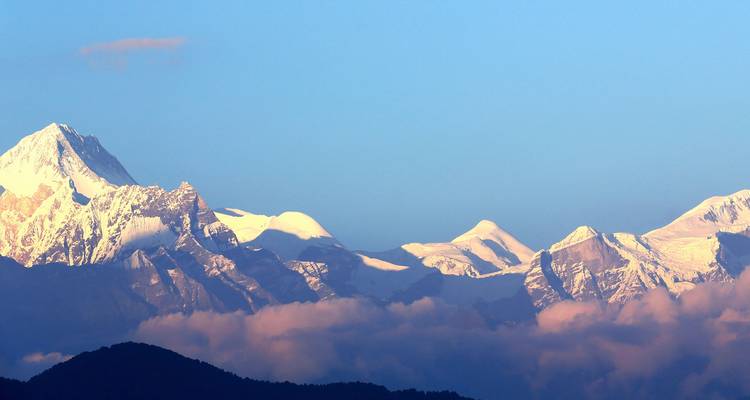 Snow-capped Annapurna range peaks glowing in warm light above soft clouds