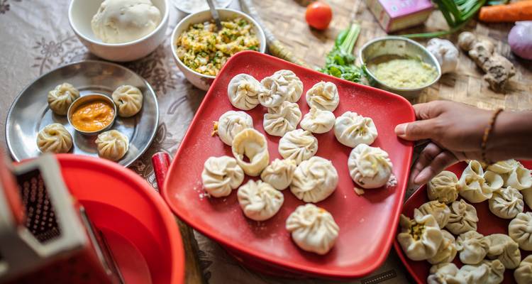 Plate of freshly made Nepali momos on a red tray surrounded by bowls of ingredients on a kitchen table