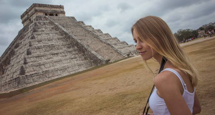 Un viajero mirando la pirámide de Kukulcán en Chichén Itzá bajo un cielo nublado.