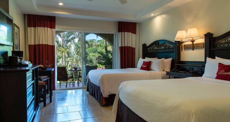 Comfortable resort bedroom with two queen beds, garden view patio and warm lighting.