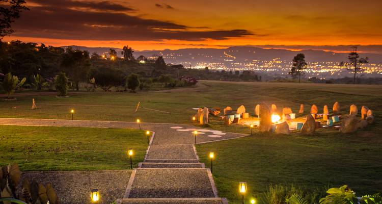 Fiery sunset over a countryside resort with a circular fire pit and distant city lights.