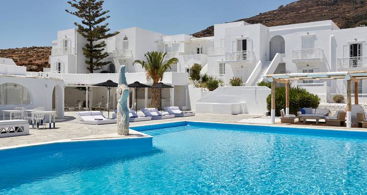 Piscina turquesa invitante enmarcada por villas cicládicas blancas, tumbonas y un telón de fondo de colina rocosa.