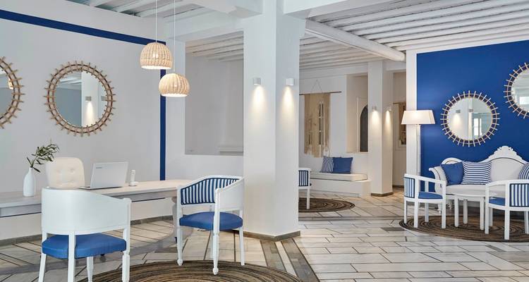 Lobby del hotel elegante decorado en blanco y azul profundo con luces de ratán, espejos redondos y pisos con baldosas.
