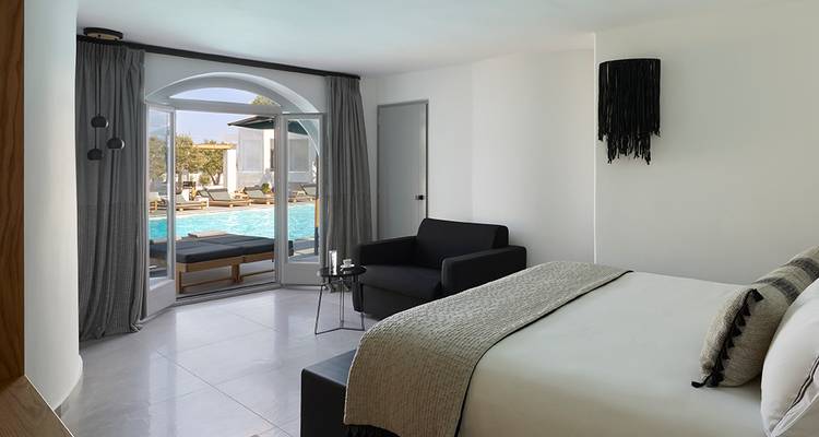 Habitación de huéspedes minimalista con tonos neutros que da a una piscina a través de puertas francesas, con un sofá oscuro y ropa de cama clara.