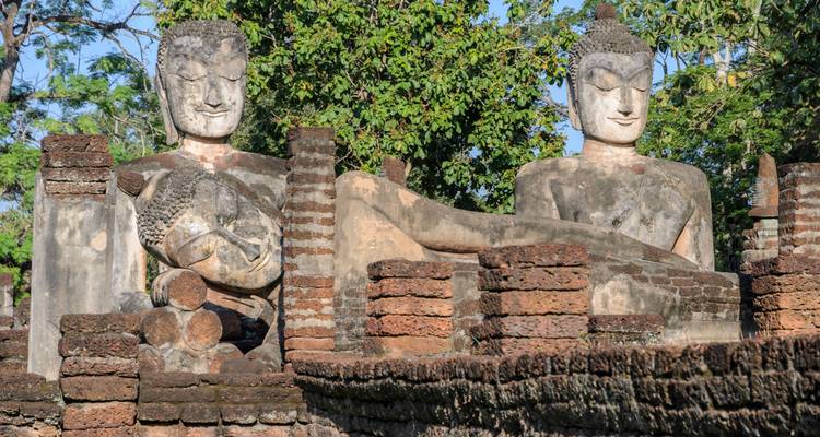 Ancient stone Buddha statues surrounded by brick structures with trees in the background.