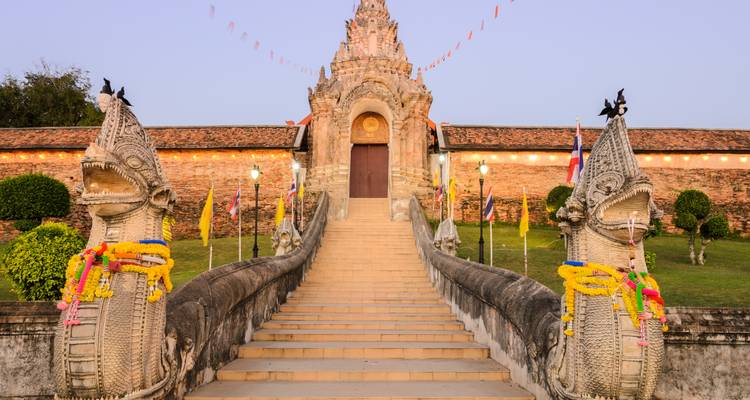 Wide staircase with ornate carvings leading to a temple entrance surrounded by greenery.