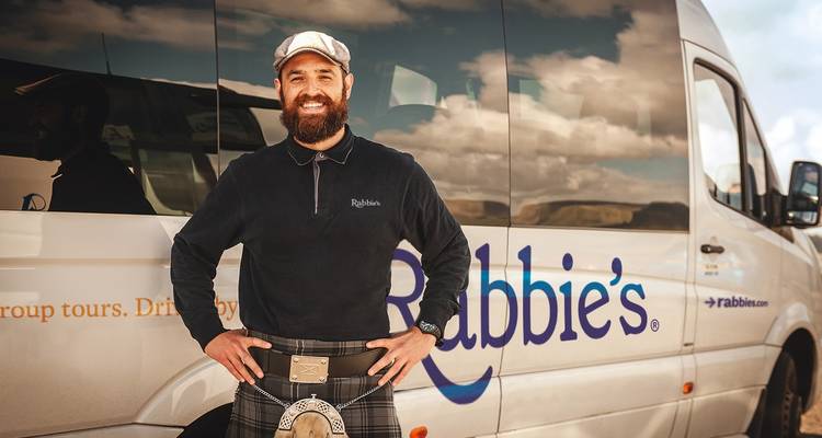 Man in traditionele Schotse kledij voor een tourbus.